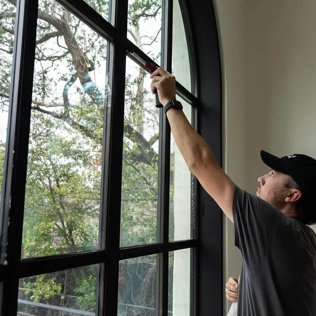 A dedicated team member of Pane'N The Glass Window Cleaning Austin LLC, cleaning an interior window with a squeegee.